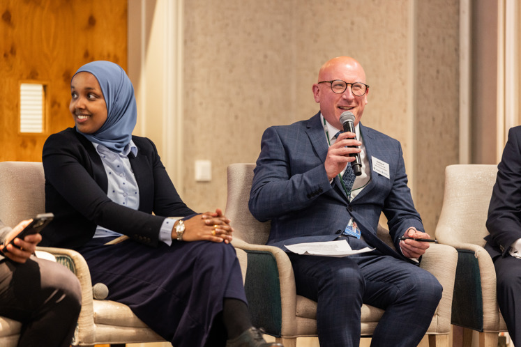 Close up, candid image of two panel presenters. David Eacott, Executive Director of Supervision at the JFSC is sat on the right, smiling with a microphone in his right hand looking out to the audience.