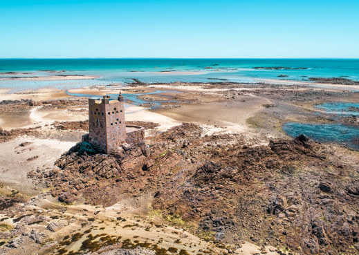 Jersey turret with sand and stony beach with patches of sea