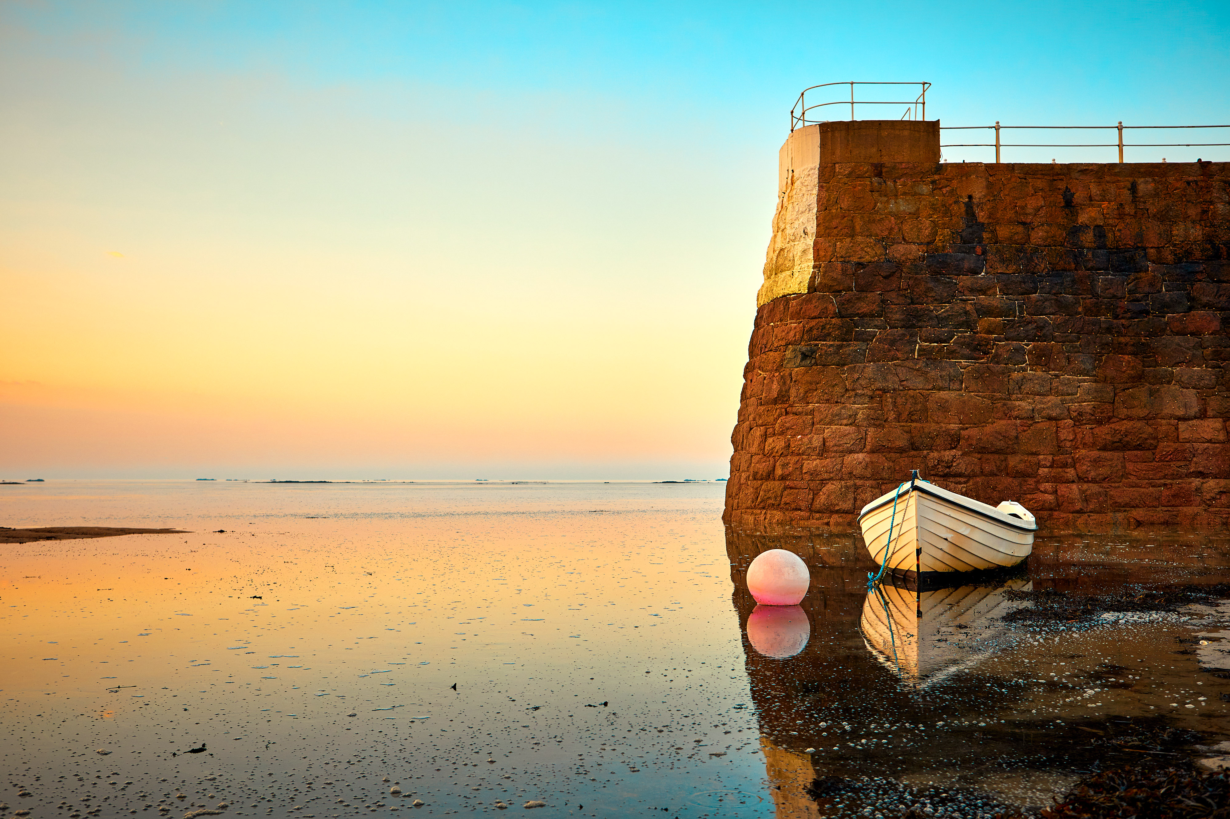 St Brelades bay in jersey with stone pier and a white boat attached to a buoy